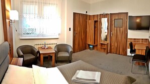A hotel room with a bed, two armchairs, a small table, a desk with a chair, a television, and a wardrobe. - Hotel Hawana (Bydgoszcz)