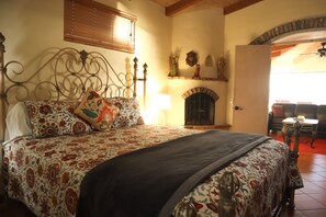 A bedroom with a large bed, a fireplace, and a dining area visible through an open door.
