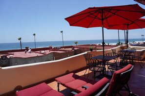 A rooftop terrace with red lounge chairs and tables, overlooking the ocean.