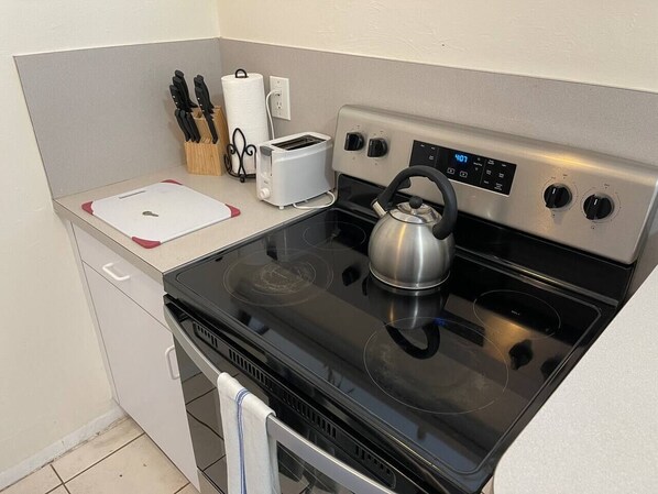 A compact kitchen with a stainless steel stove, a kettle, a toaster, and a knife block.