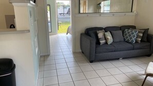 A living room with a grey sofa, a white cabinet, and a tiled floor. - #6 Heated Pool, Private Patio & Grill, 1BR+sunroom (Fort Lauderdale)