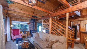 A cozy cabin interior with a wooden staircase, a sofa, a coffee table, and a red chair.