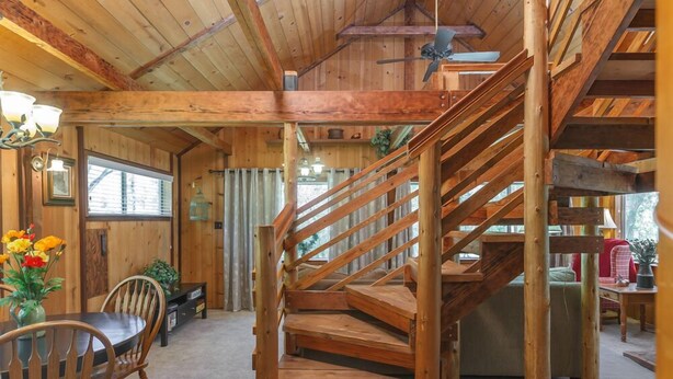 A wooden interior with a spiral staircase, a dining area with chairs and a table, and a ceiling fan.