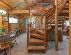 A wooden interior with a spiral staircase, a dining area with chairs and a table, and a ceiling fan.