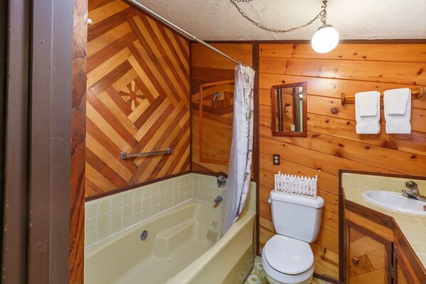 Un baño de cabaña de madera con bañera, inodoro y lavabo.