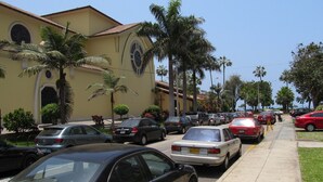 Una strada fiancheggiata da auto parcheggiate e palme, con un edificio dalla facciata gialla e finestre ad arco.