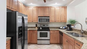 A kitchen with wooden cabinets, stainless steel appliances, granite countertops, and a ceiling fan.