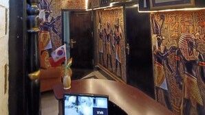 Ett rum med egyptiskinspirerad inredning, inklusive väggdekorationer och en tv-skärm som visar bilder från övervakningskameror.