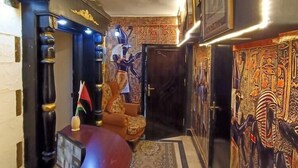 Ett rum med ett böjt skrivbord i trä, en mönstrad matta och väggdekorationer med egyptiskt tema.
