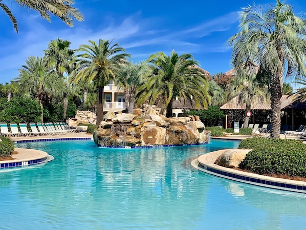 A swimming pool with a rock waterfall, surrounded by palm trees and lounge chairs.