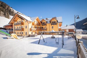 A multi-story building with balconies, a ski slope, and a swing set in a snowy environment. - Hotel Tolderhof (San Candido)