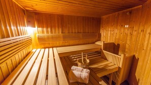 Sauna, jossa on puiset lauteet ja yksi penkkimäinen lauderivi, puinen ämpäri ja pyyhe.