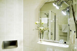 A bathroom with a mirror, a towel rack, a glass vase with flowers, and a hairdryer.