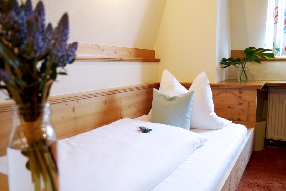 A bedroom with a wooden headboard, a white bed with pillows, a vase with flowers, and a radiator.