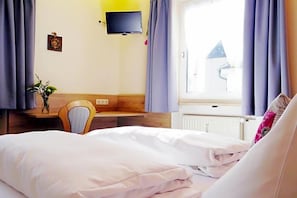 A hotel room with a bed, a desk, a chair, a television mounted on the wall, and a window with curtains. - Grader (Neustadt an der Waldnaab)