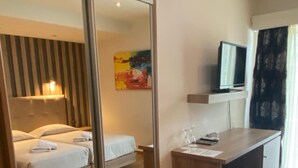 A hotel room with a bed, a desk, a television, and a painting on the wall.