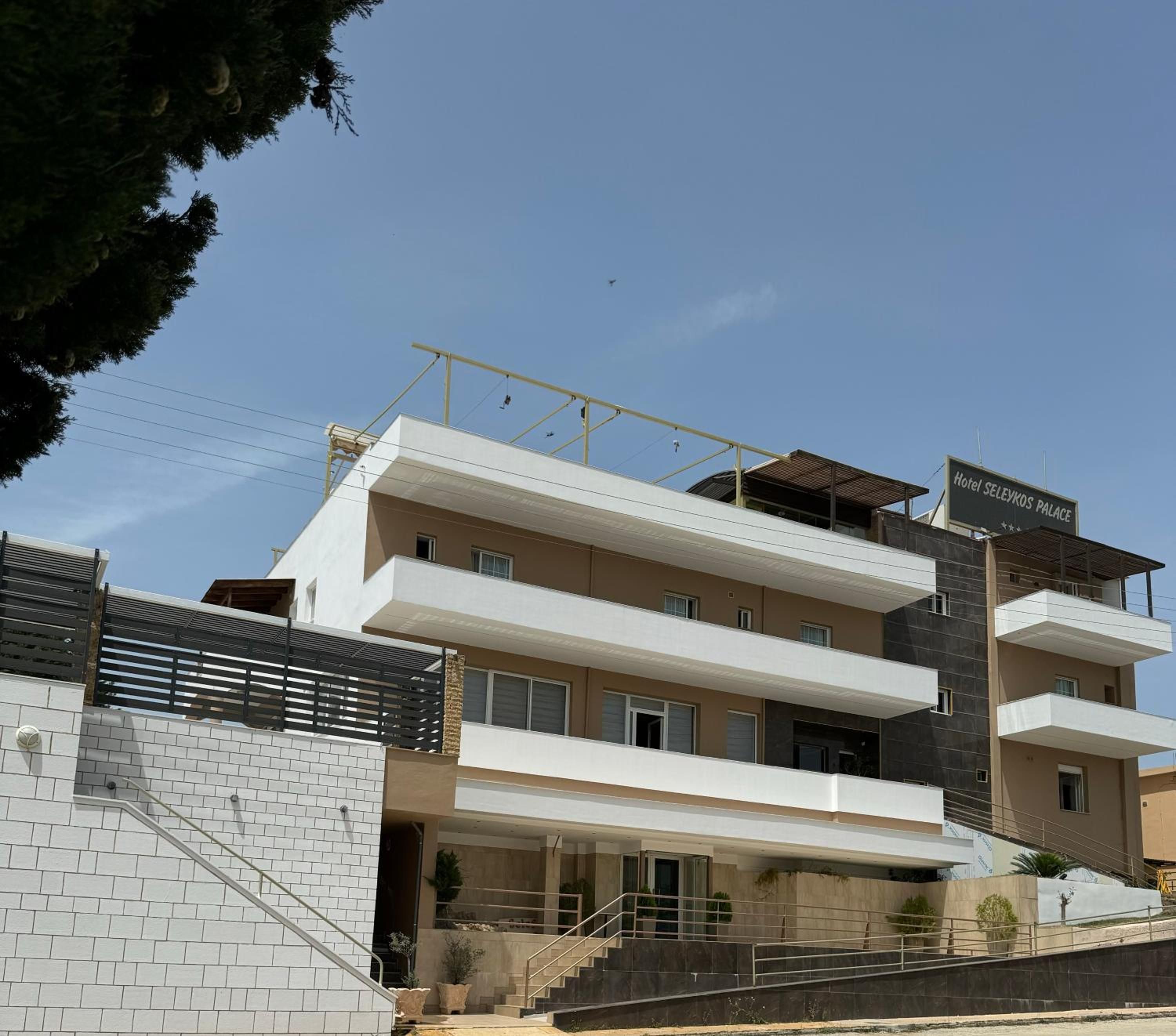 A multi-story hotel with a modern architectural design, featuring a prominent entrance with a staircase and a balcony on the upper floors.