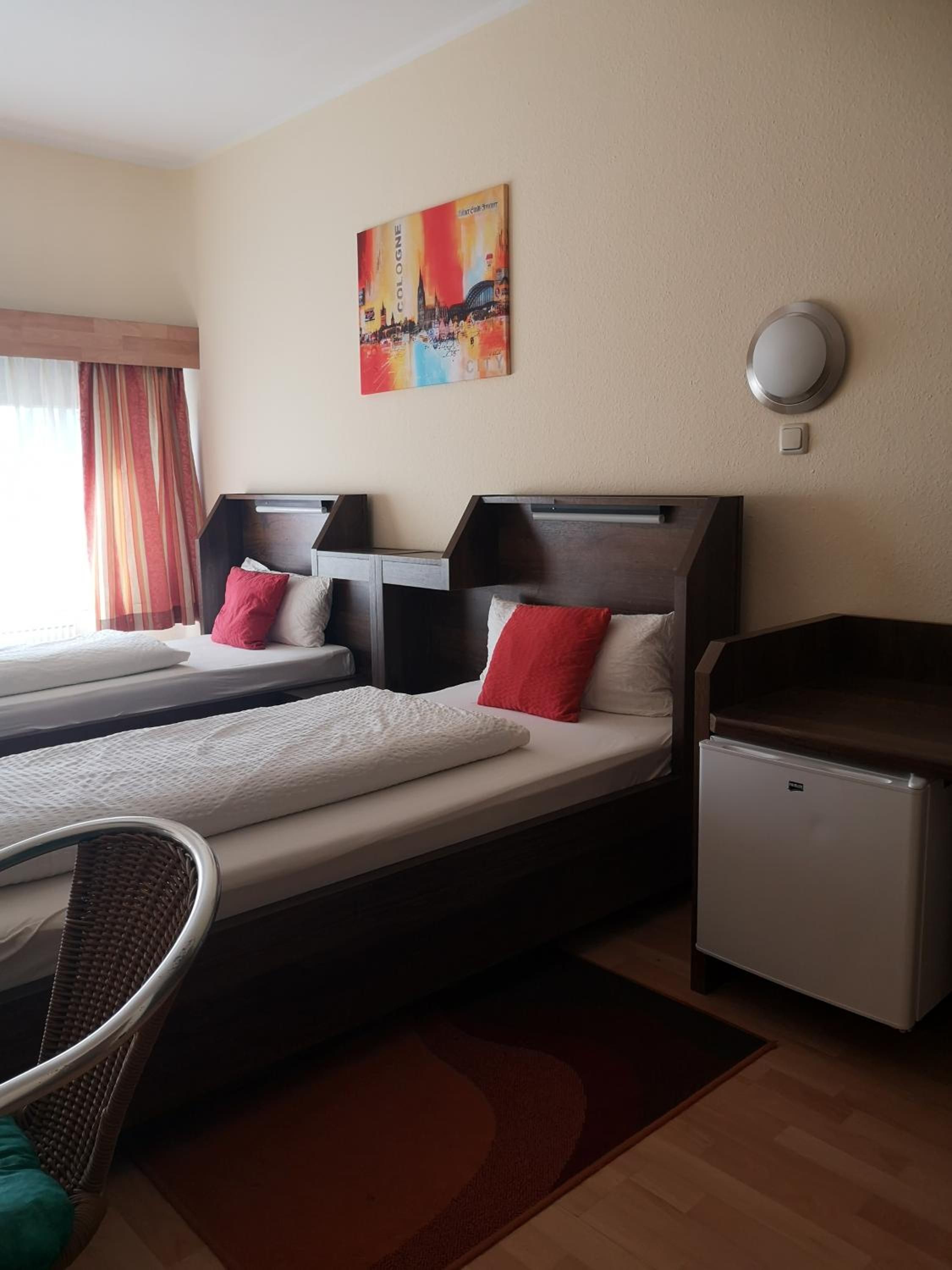 A hotel room with two beds, a small refrigerator, a chair, and a painting on the wall.