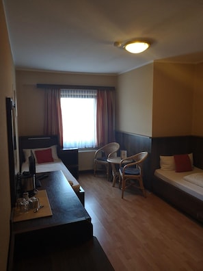 A hotel room with a bed, a desk, two chairs, a window with curtains, and a ceiling light.