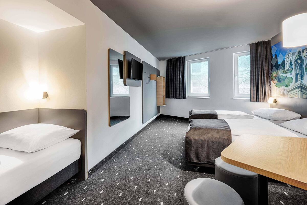 Moderni hotellihuone, jossa on sänky, työpöytä, tuoli, televisio ja taulu seinällä.