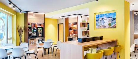 A modern cafe with a yellow and white color scheme, featuring a bar area with yellow stools, white chairs, and a wooden counter.