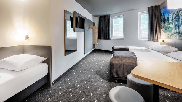 A modern hotel room with a bed, a desk, a chair, a TV, and a painting on the wall. - B&B HOTEL Bonn-West (Bonn)