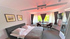 A bedroom with a bed, a desk, two chairs, a television, and a window with curtains.