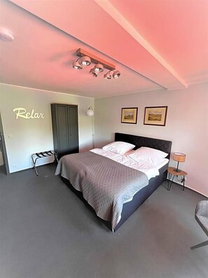 A bedroom with a bed, a wardrobe, a bedside table, a lamp, and a wall-mounted shelf.