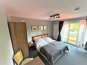 A hotel room with a bed, bedside table, lamp, and a view of the outdoors.
