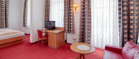 Una habitación de hotel con una cama, un escritorio, una silla, un sofá rojo y una mesita redonda.
