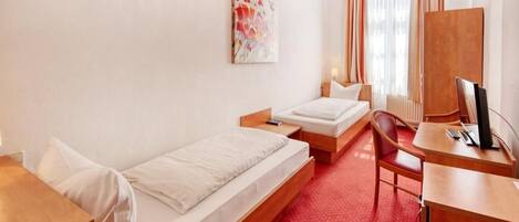 A hotel room with two beds, a desk, a chair, a TV, and a painting on the wall.