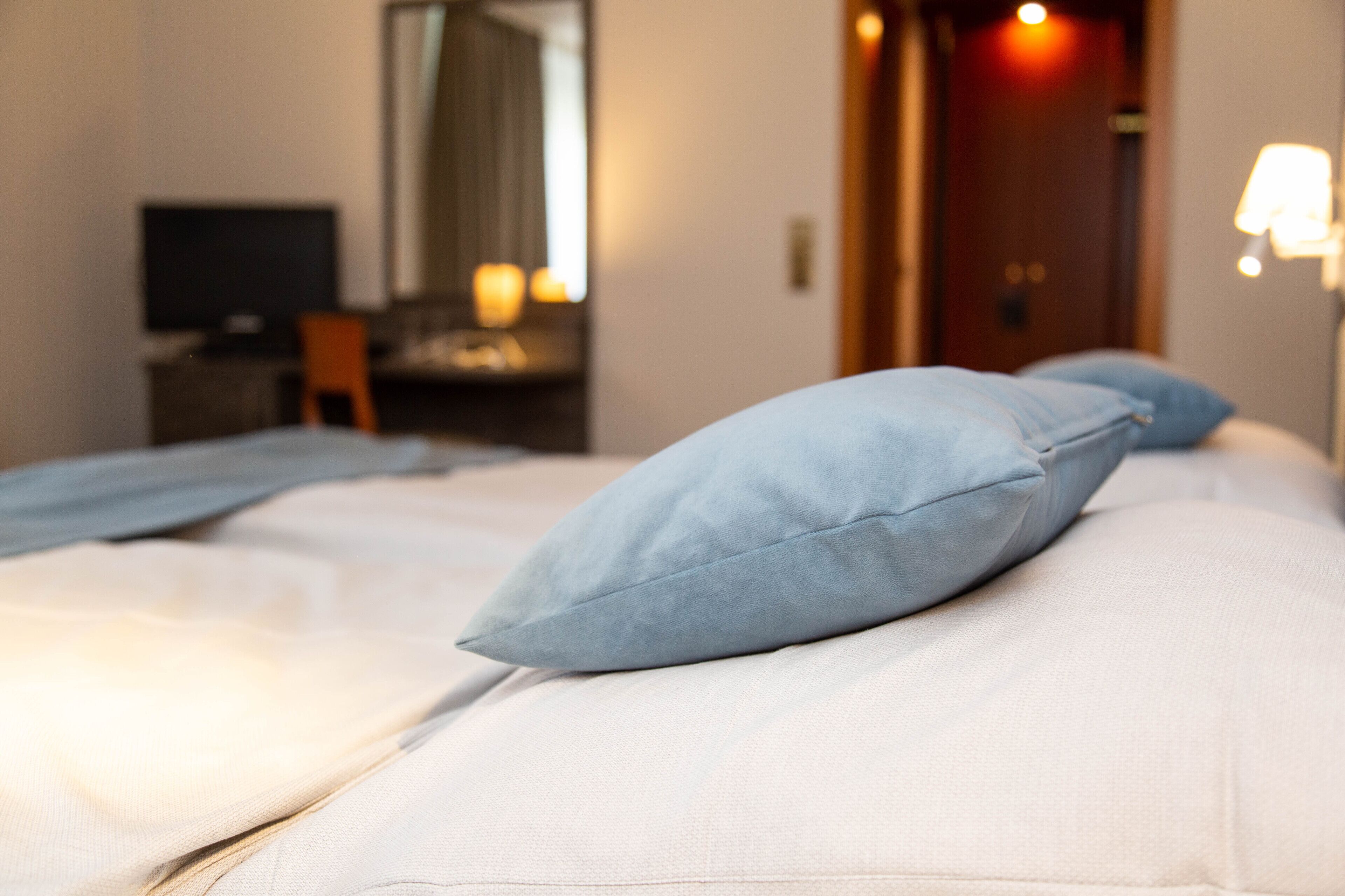 Una cama bien hecha con almohadas azules y una colcha blanca en una habitación de hotel.