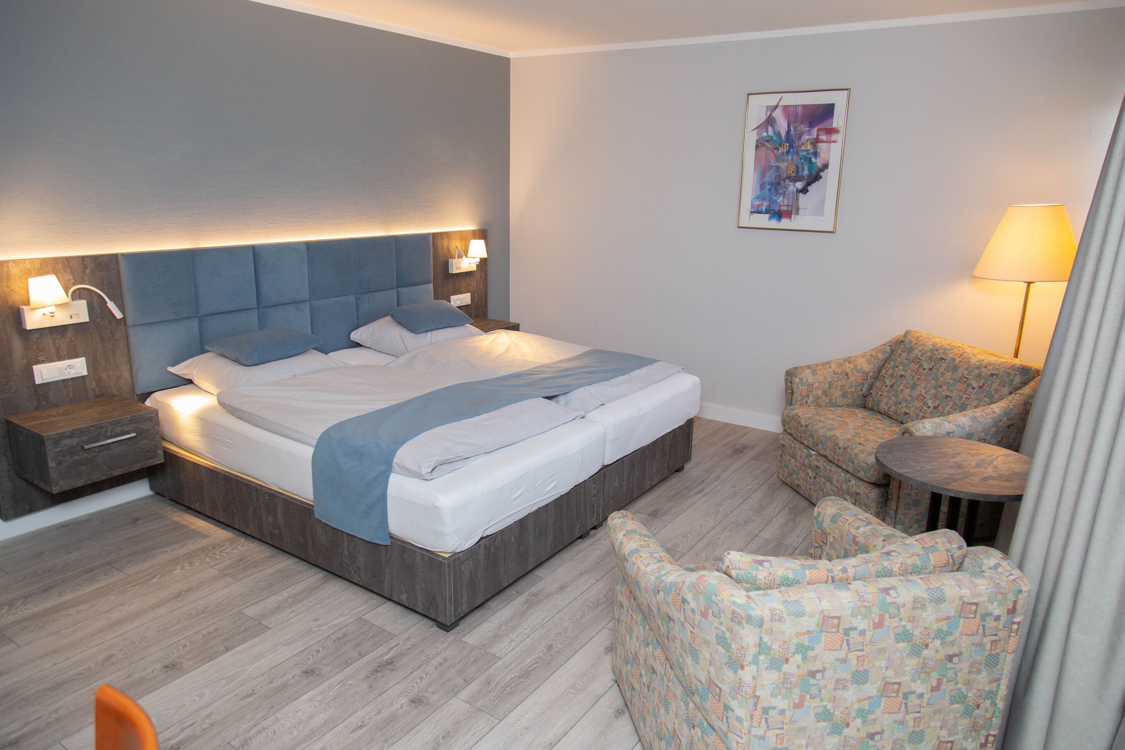 Una habitación de hotel moderna con una cama grande, un sofá, una mesita y una mesita de noche con lámpara.