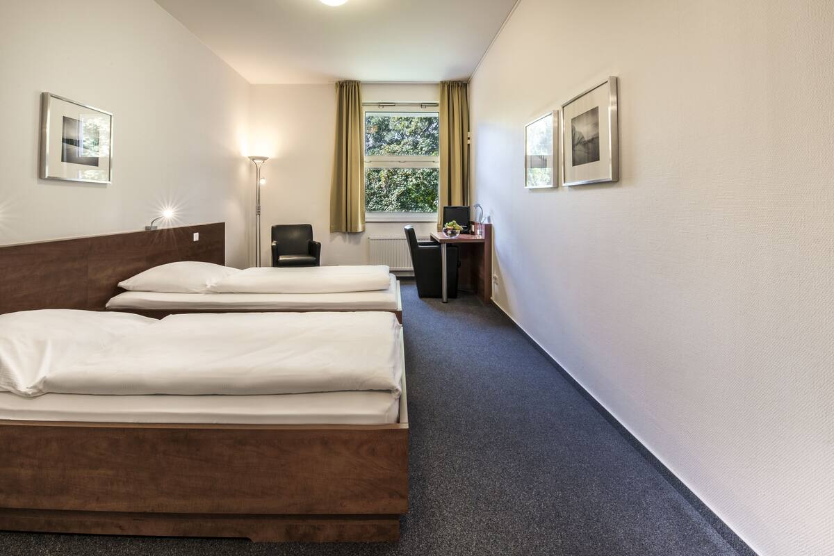 A hotel room with a double bed, a desk with a chair, a lamp, and two framed pictures on the walls.