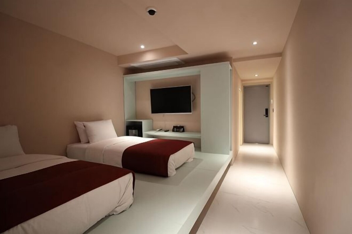 Une chambre d’hôtel avec deux lits, un téléviseur à écran plat et un couloir menant à une autre chambre.