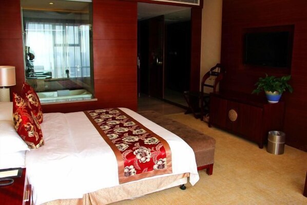 A hotel room with a large bed, a desk, a chair, a TV mounted on the wall, and a potted plant. - Guest Hotel of Luohe (Luohe)