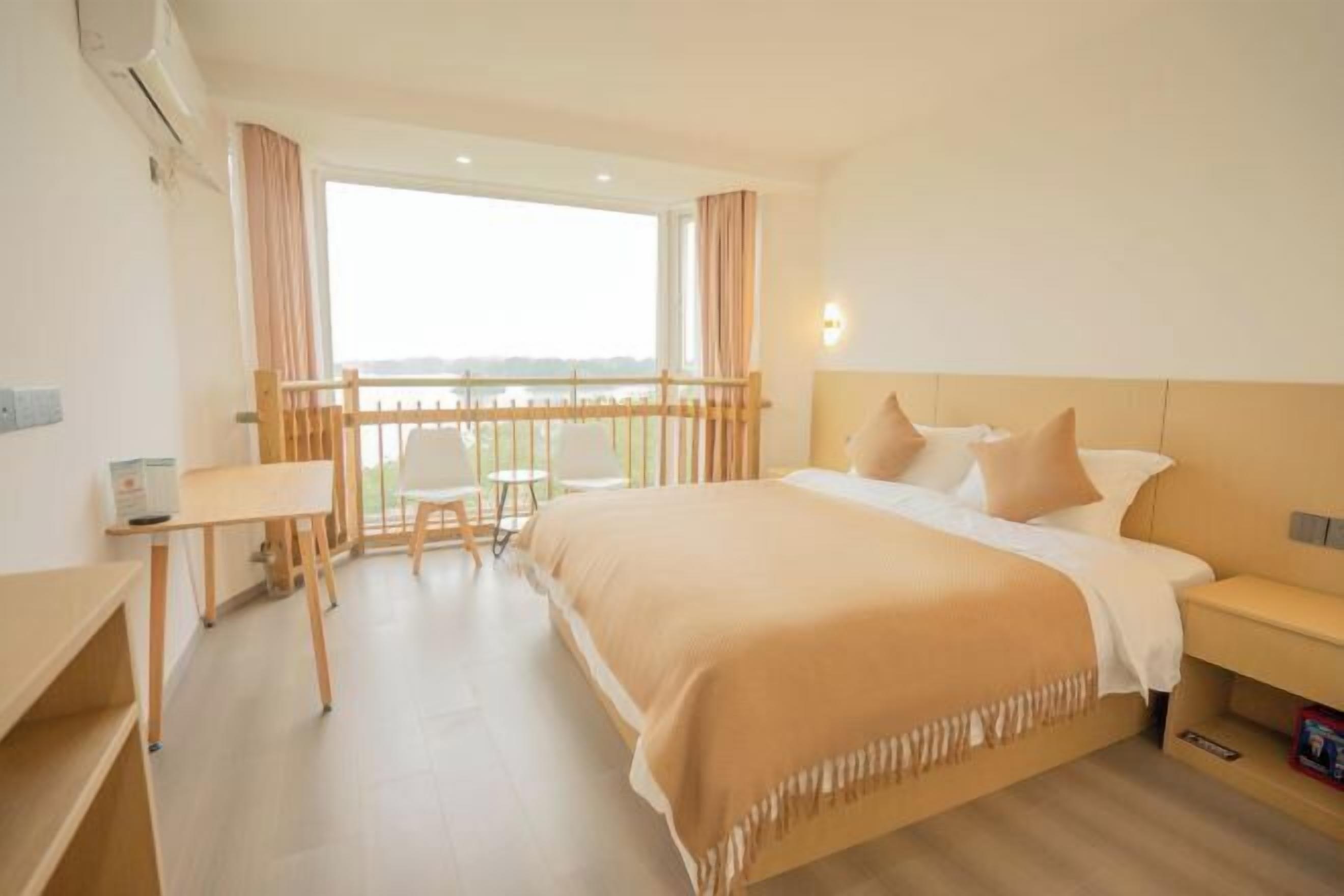 A hotel room with a bed, bedside table, chair, and a balcony with a railing.