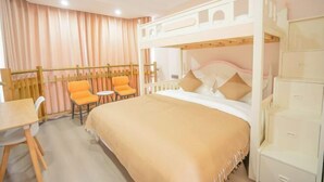 Een stapelbed met een wit hoofdeinde, een klein tafeltje, twee oranje stoelen en een witte kledingkast.