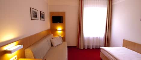 Habitación de hotel con sofá, cama, escritorio, televisión montada en la pared y ventana con cortinas.