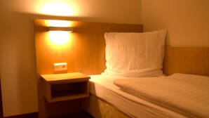 A hotel room with a single bed, a nightstand, and a wall-mounted light. - Hotel Jacobsberg (Oschersleben)