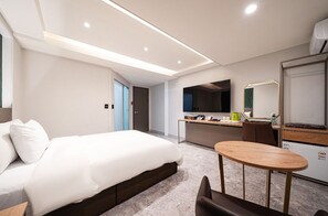A modern hotel room with a bed, a small round table, a kitchenette, and a bathroom.