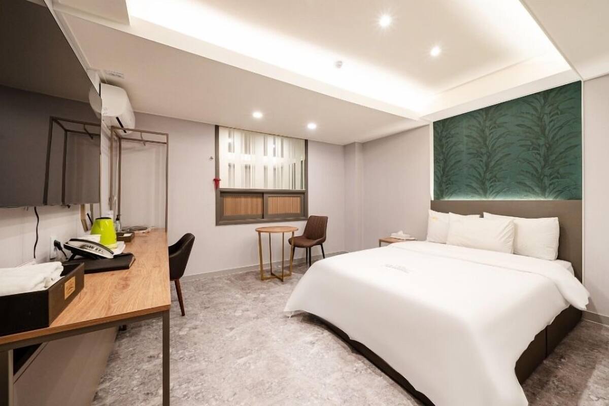 A modern hotel room with a large bed, a desk with a chair, a small table, and a window.