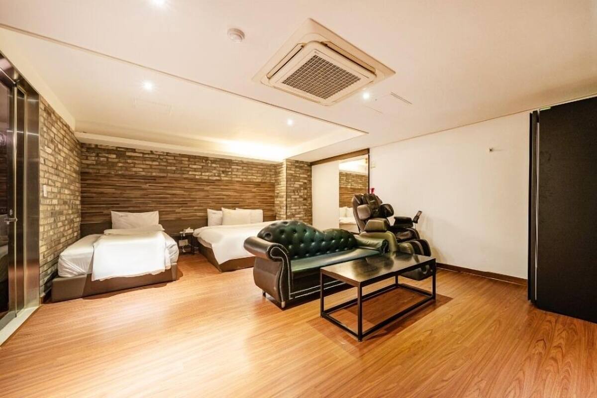 A modern hotel room with two beds, a massage chair, a small table, and a black wardrobe.
