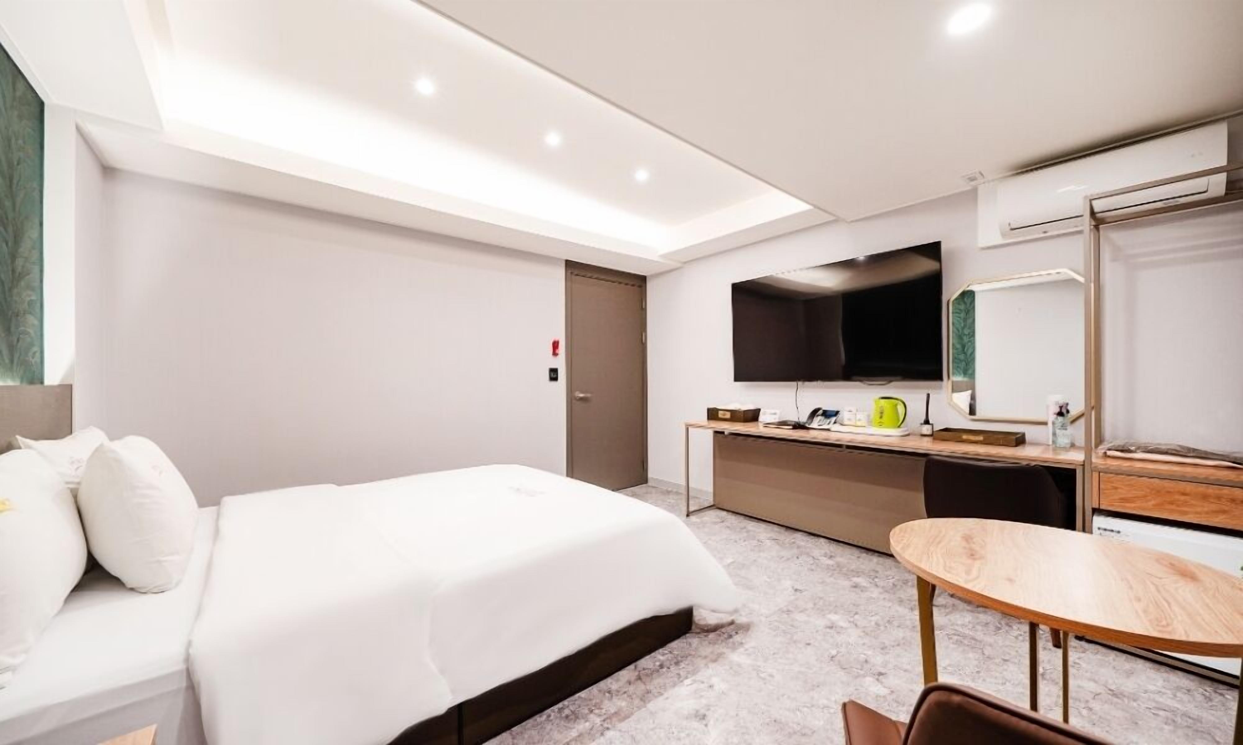Una habitación de hotel moderna con una cama grande, un escritorio, una silla, un televisor de pantalla plana y un espejo.