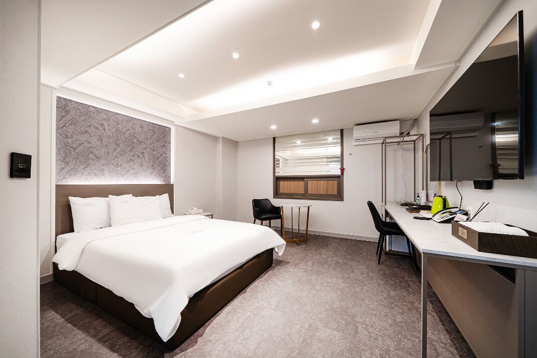 Une chambre d’hôtel avec un grand lit, un bureau avec une chaise, une petite table et une fenêtre avec des stores.