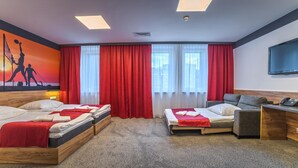 A hotel room with two beds, a sofa, a TV, and a large window with red curtains. - Hotel Scout (Czestochowa)