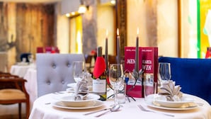 Una mesa de comedor dispuesta con platos, cubiertos, copas y velas, con libros y una botella de vino sobre la mesa.