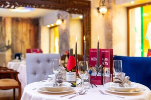 Una mesa de comedor dispuesta con platos, cubiertos, copas y velas, con libros y una botella de vino sobre la mesa.