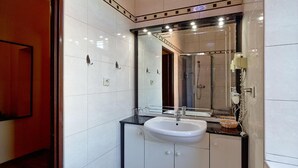 Un baño moderno con un espejo grande, un lavamanos blanco y una zona de ducha.