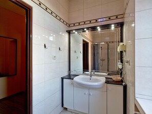 Un baño moderno con un espejo grande, un lavamanos blanco y una zona de ducha.